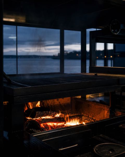 Open houtvuur onder de grill met de rivier op de achtergrond.