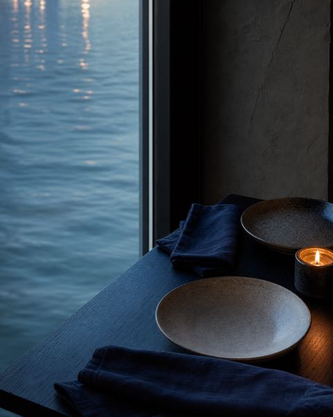 Tafel voor twee met donkerblauw linnen naast het water.